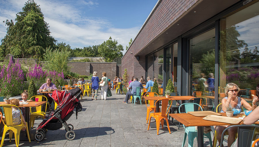 People sitting at tables outside a cafe in the sun talking
